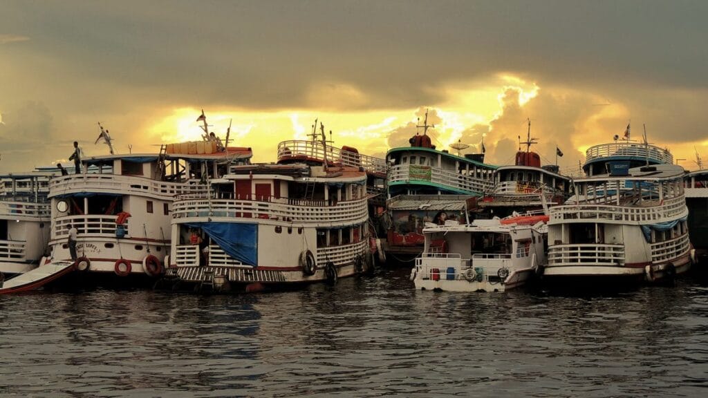 Voo para o Motor Yacht Tucano: chegar a Manaus antes de o barco zarpar 2 Barcos regionais amazônicos atracados no Rio Negro, em Manaus, ao pôr do sol